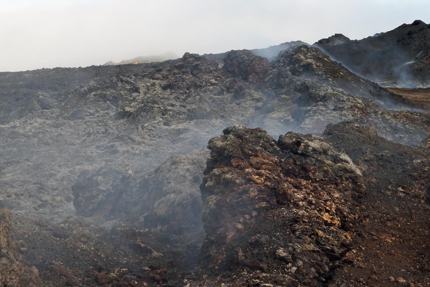Das Bild zeigt einen schwarz-roten Lavastrom am Mývatn, der in Rauch gehüllt ist.