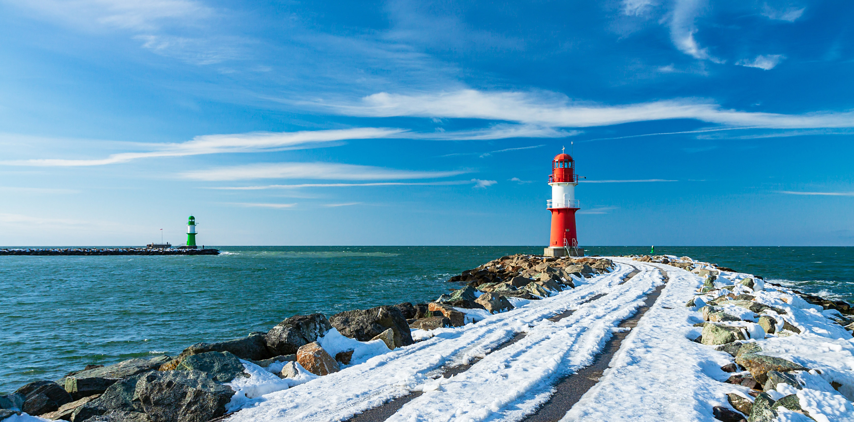 Schneebedeckte Mole, im Vordergrund rotweißer Leuchtturm, blauer Himmel, Meer, im Hintergrund links grünweißer Leuchtturm.